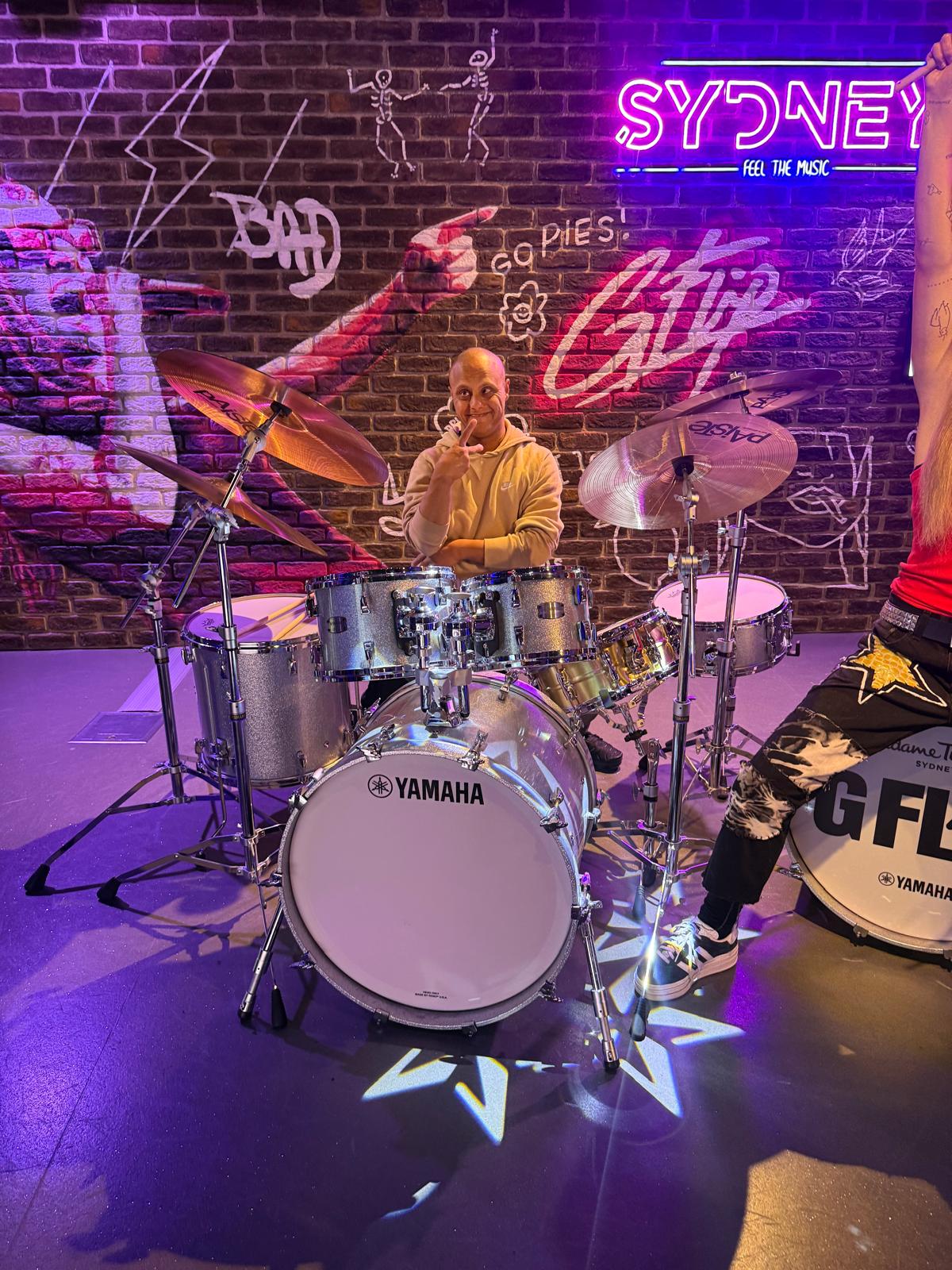 A participant sitting behind a drum kit at a music exhibit