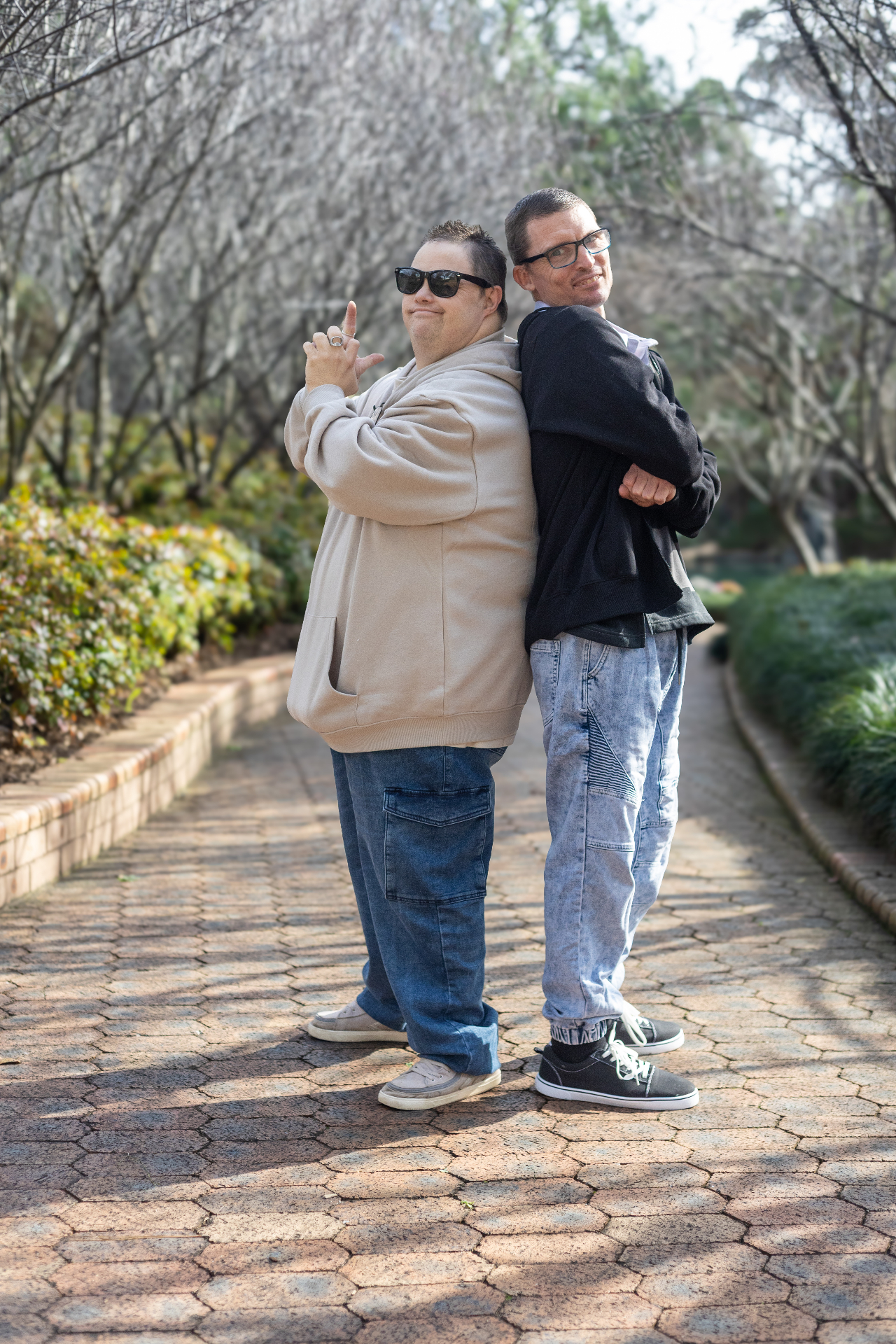 Two mates posing back to back on a tree-lined path